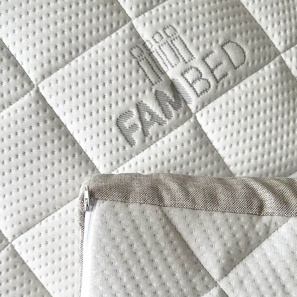 Gros plan sur la housse blanche matelassée du surmatelas, avec le logo FAMBED tissé dans le tissu