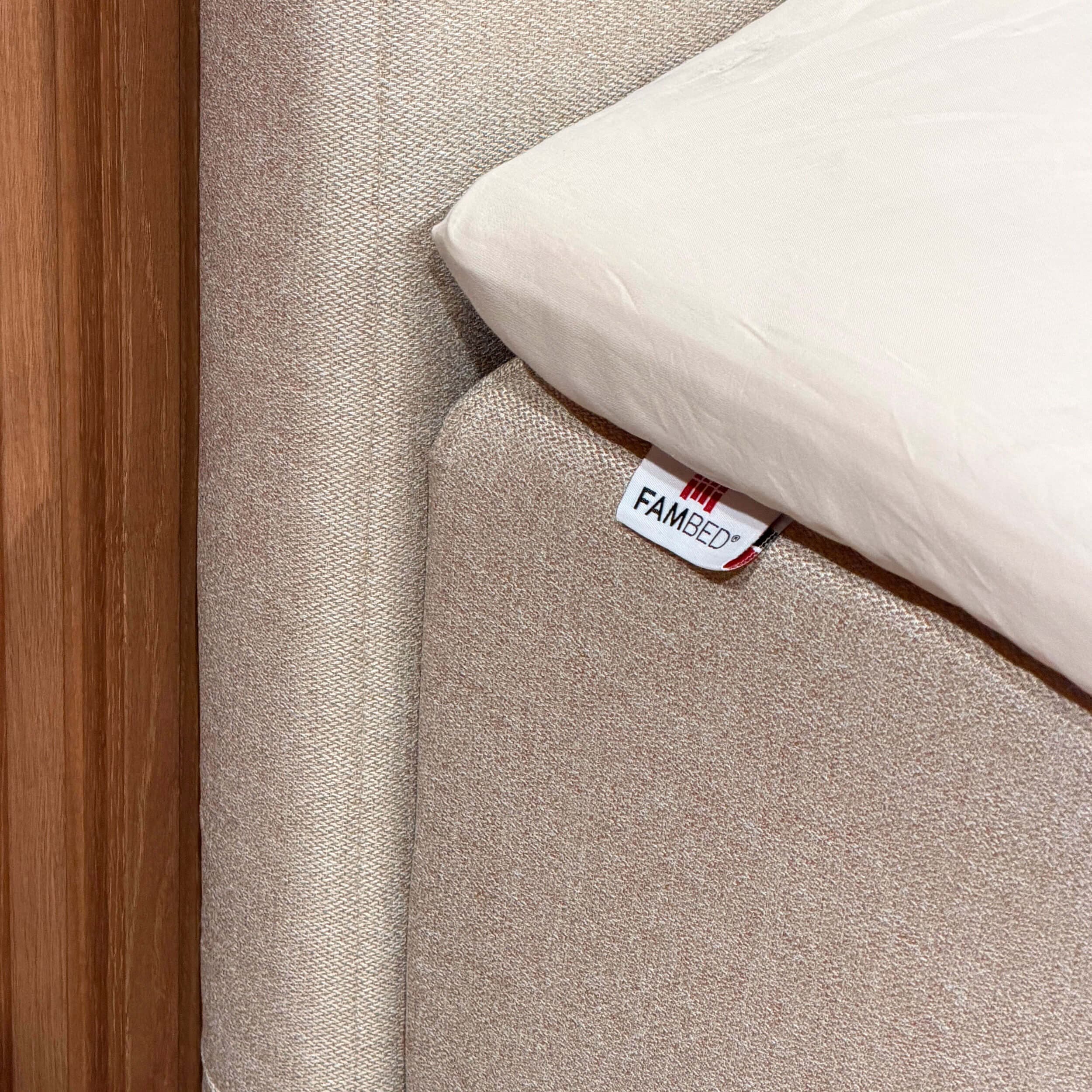 Gros plan sur la housse beige enveloppant le coin du lit, avec l’étiquette FAMBED et un drap blanc par-dessus