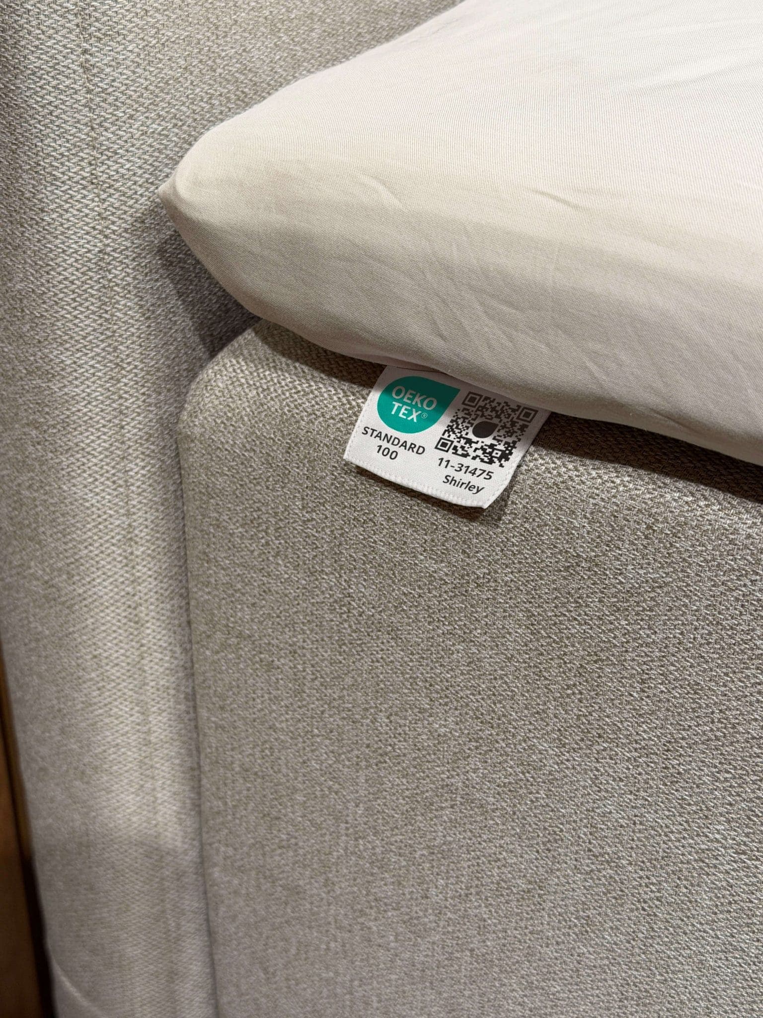Étiquette OEKO-TEX® STANDARD 100 cousue sur le tissu beige du lit, sous le drap