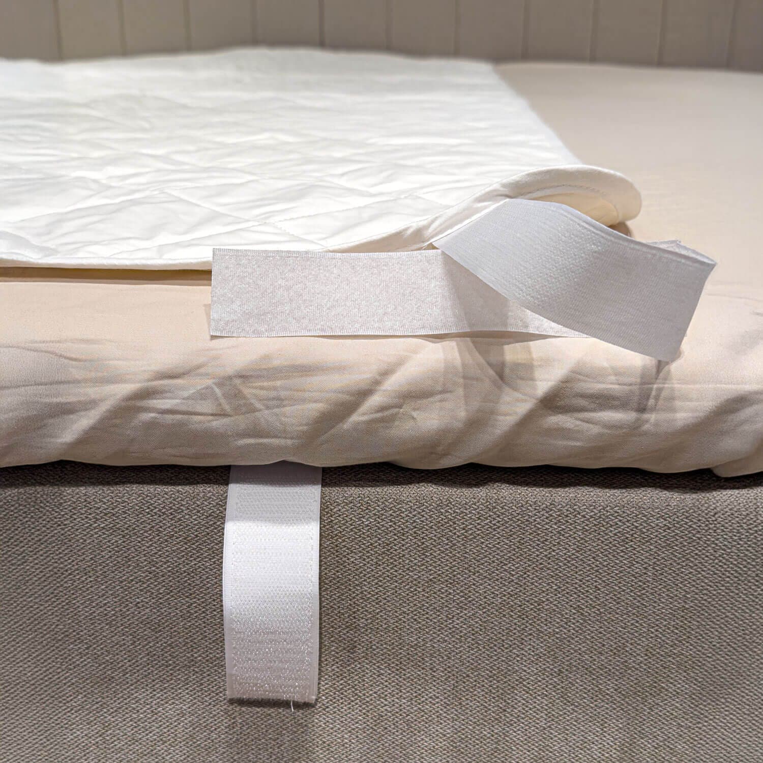 Coin du protège-matelas blanc matelassé replié pour dévoiler la bande autoagrippante autour du bord du lit