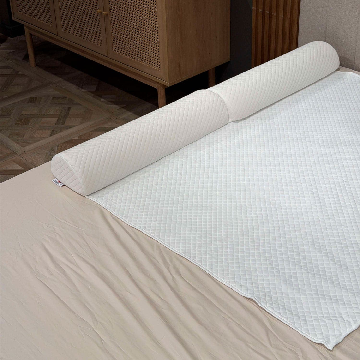 Barrière de lit matelassée en mousse installée sous la housse blanche du surmatelas, le long du bord du lit