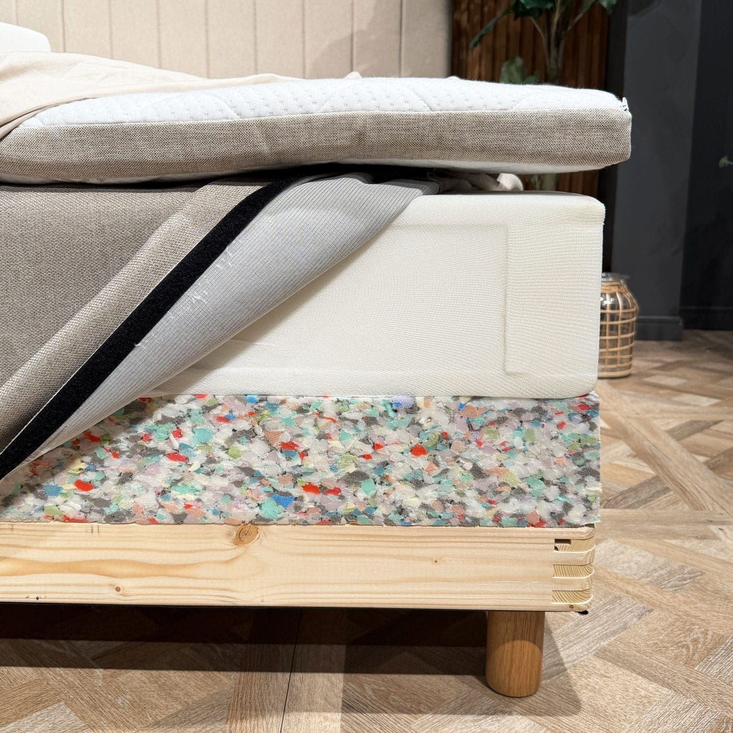 Couches du lit dévoilées dans un angle : surmatelas, matelas à ressorts avec housse ouverte et rebord en mousse du sommier au-dessus du cadre en bois