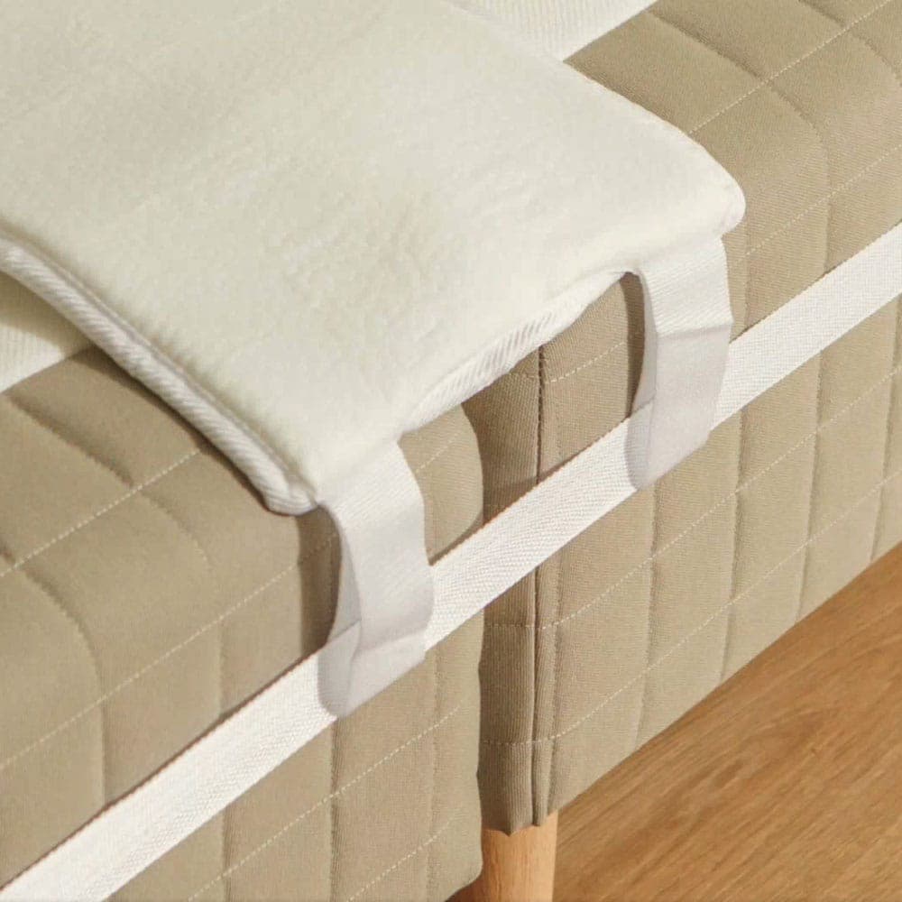 Cale de matelas blanche posée sur la jonction entre deux matelas et maintenue en place par la sangle de lit