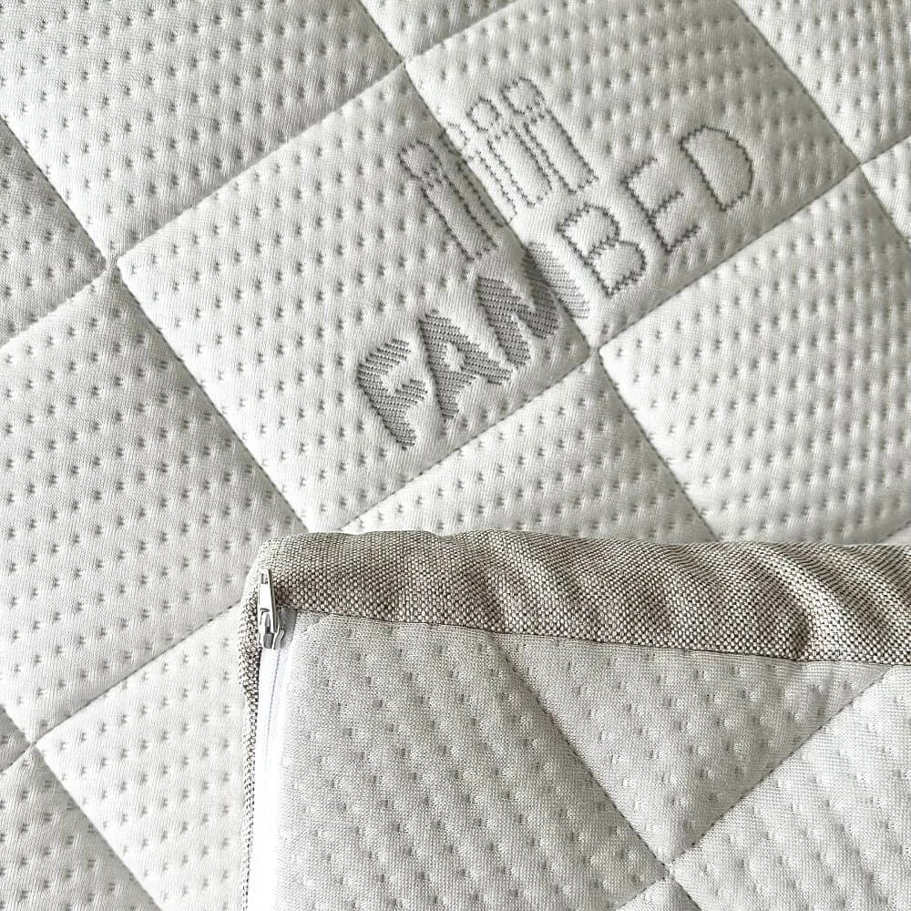 Gros plan sur la housse blanche matelassée du surmatelas, avec le logo FAMBED tissé dans le tissu