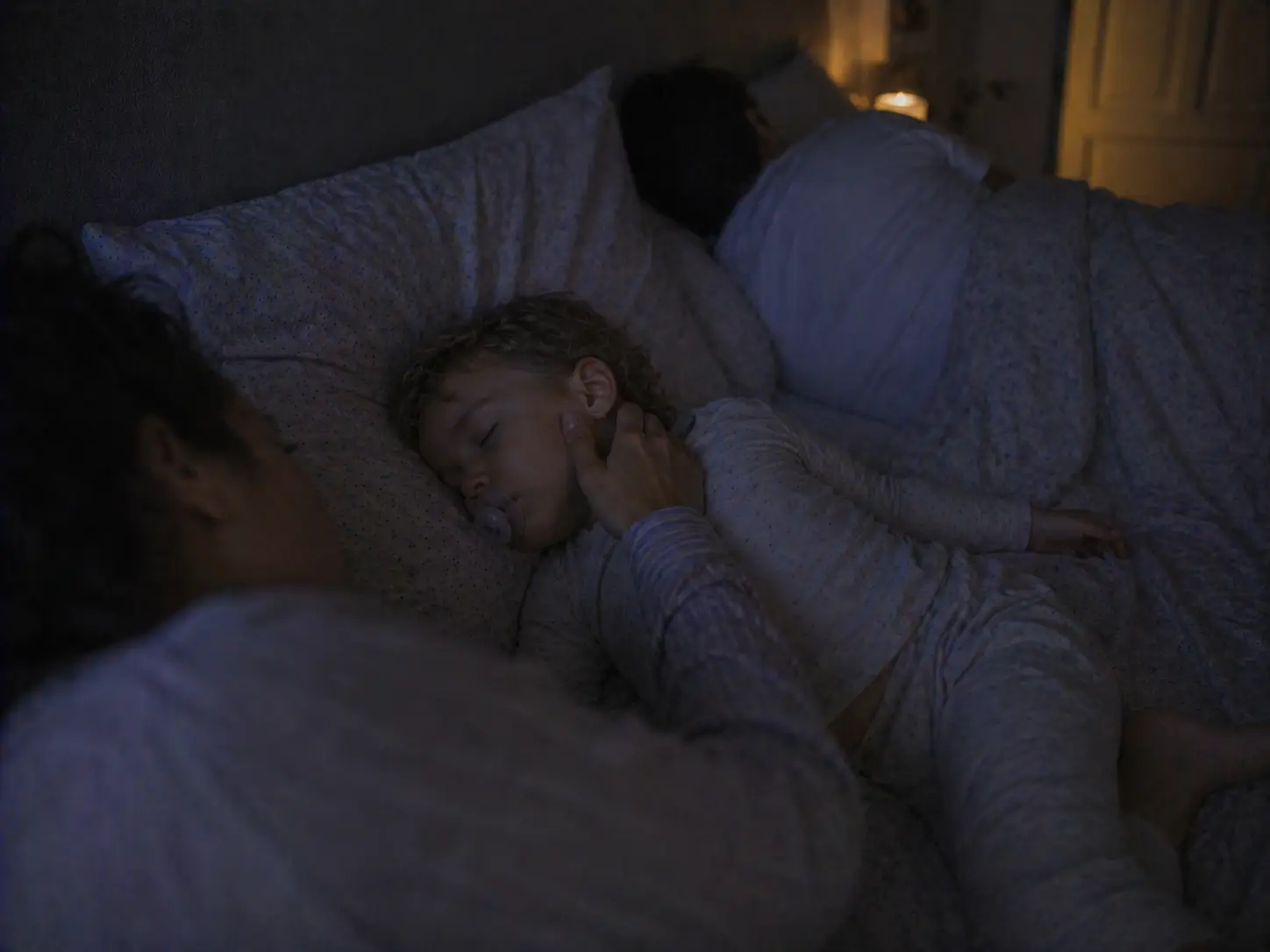 Une mère caresse doucement la joue de son enfant endormi dans le lit familial, la nuit