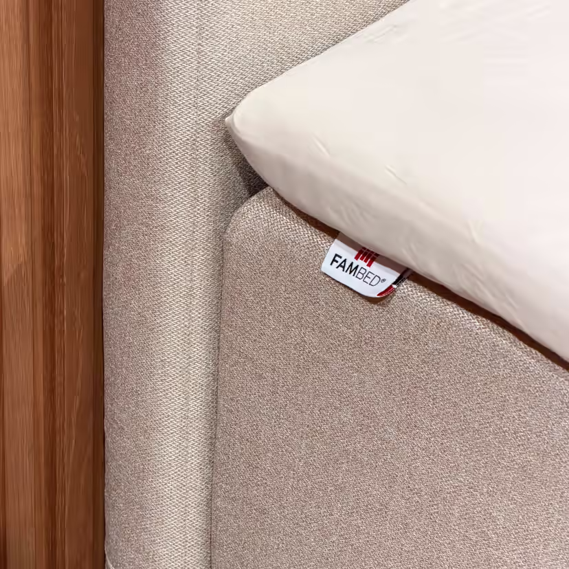 Gros plan sur la housse beige enveloppant le coin du lit, avec l’étiquette FAMBED et un drap blanc par-dessus