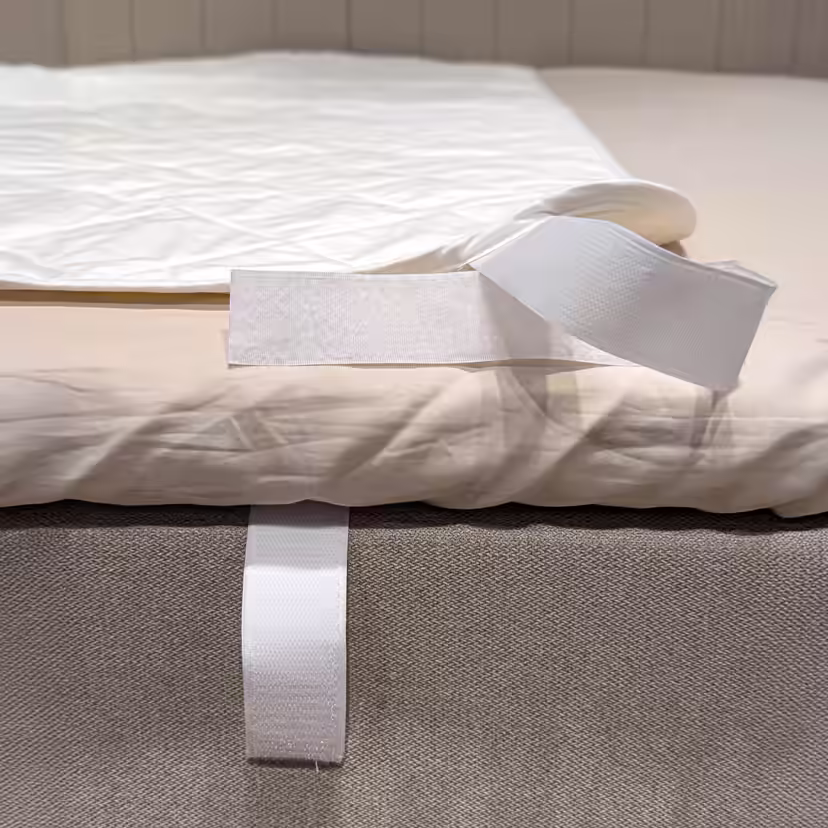 Coin du protège-matelas blanc matelassé replié pour dévoiler la bande autoagrippante autour du bord du lit