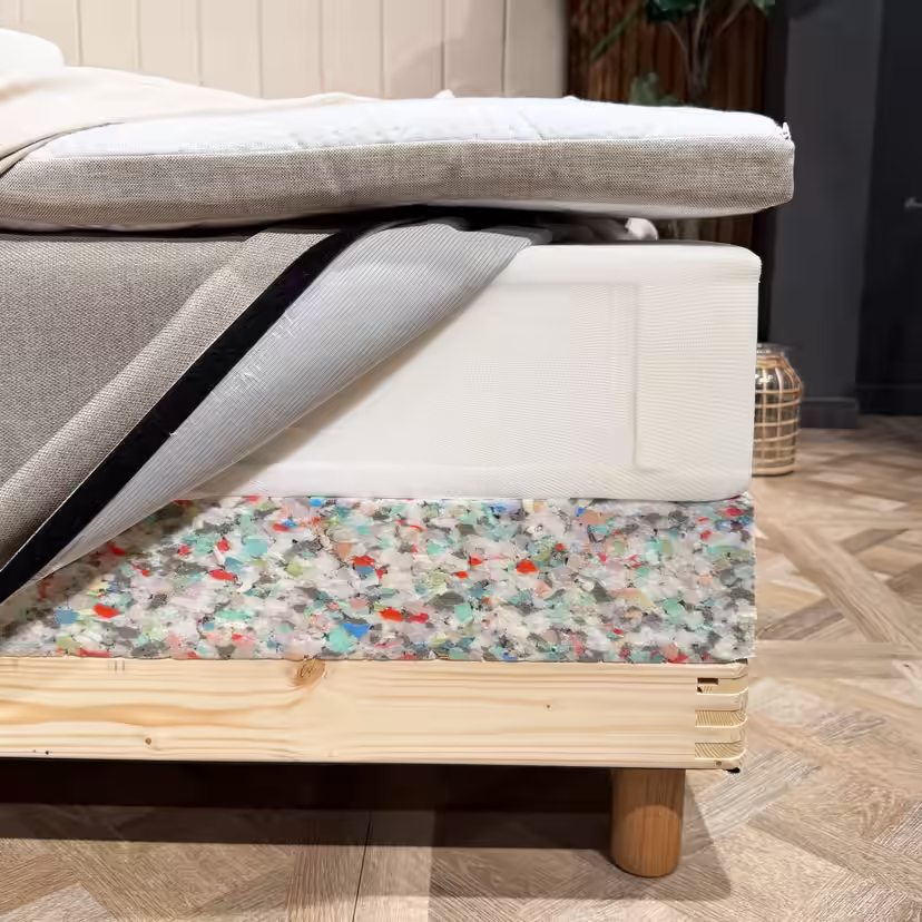 Couches du lit dévoilées dans un angle : surmatelas, matelas à ressorts avec housse ouverte et rebord en mousse du sommier au-dessus du cadre en bois